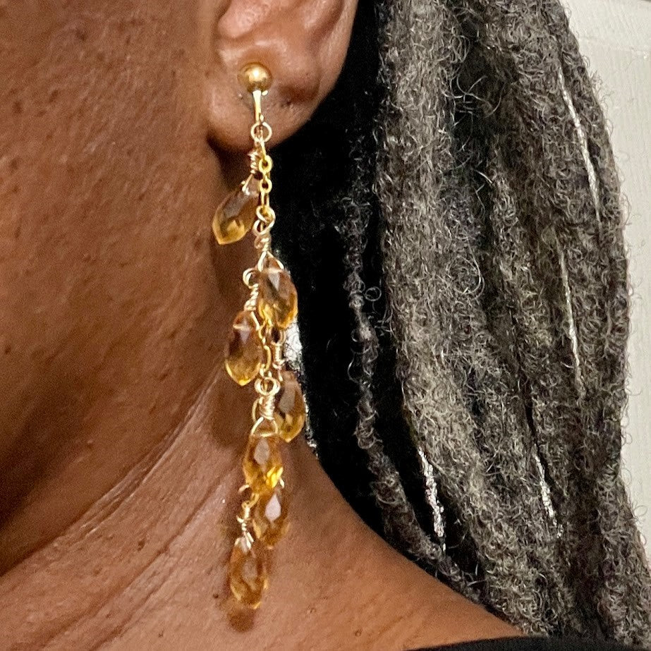 Side profile of model wearing screwback, clip-on earrings. Gold-plated brass throughout. Seven faceted topaz briolettes dangling from 6" link chain.